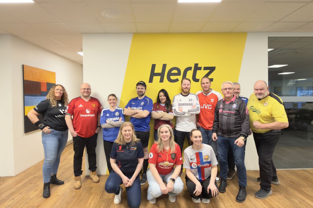 Starfsfólk Hertz á Íslandi í fótboltatreyjum fyrir framan Hertz-vegginn á skrifstofunni